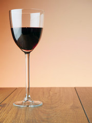 One glass of red wine on a wooden table, warm background color. Vertical image.