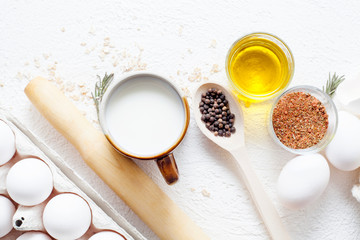 Ingredients for cooking on a white background in the composition, including milk, eggs, spices and olive oil with black pepper in polka dots. The concept of cooking and recipes.