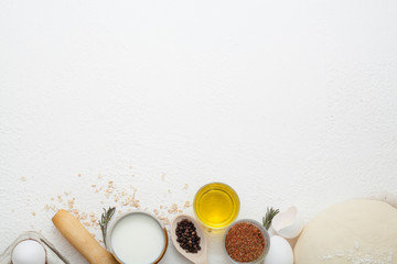 Ingredients for cooking on a white background, including milk, eggs, spices and dough with olive oil and black pepper in polka dots, with copy space. The concept of cooking and recipes.