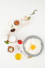 Broken egg on flour in a plate, Ingredients for cooking on a white background, in a beautiful composition, including milk, eggs, spices and olive oil with black pepper. The concept of cooking, recipes