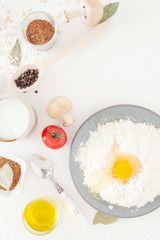 Broken egg on flour in a plate, Ingredients for cooking on a white background, in a beautiful composition, including milk, eggs, spices and olive oil with black pepper. The concept of cooking, recipes
