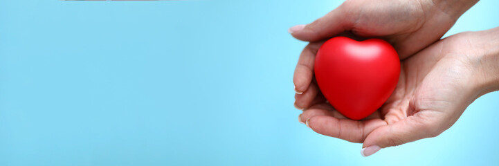 Woman hand hold red toy heart in hand against blue background closeup. Charity people concept