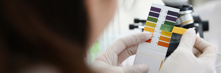 Female chemist holding litmus paper in hands. Analyzes ph test in a chemical laboratory. Chemistry...