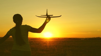 Fototapeta na wymiar children play toy airplane. Happy girl runs with a toy airplane on a field in the sunset light. teenager dreams of flying and becoming pilot. the girl wants to become pilot and astronaut.