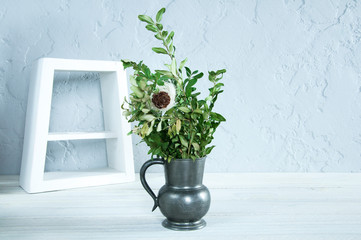 Antique vase with green plants flowers. White frame. On wooden background