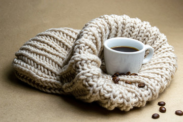white cup with coffee and coffee beans on a beige knitted hat on a beige background