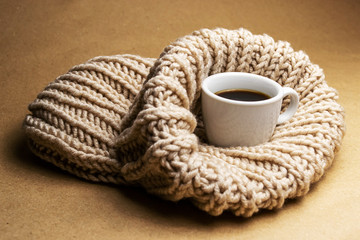 white cup with coffee on a beige knitted hat on a beige background