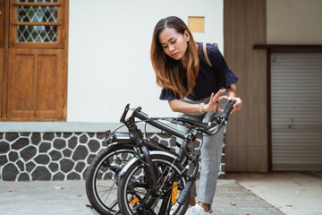 Fototapeta na wymiar asian young woman trying fold her folding bike to prepare go to work in front the house