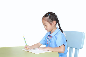 Intend little kid girl in school uniform writing on notebook at desk isolated over white background.
