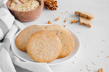 Freshly baked oatmeal cookies with raisins and nuts on a white plate on a light stone background. Rustic style Horizontal orientation.
