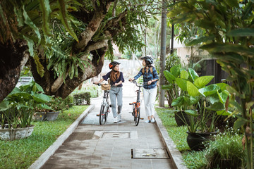 Two Asian women chatting and walking while walks with folding bikes enjoy bicycle sports before work