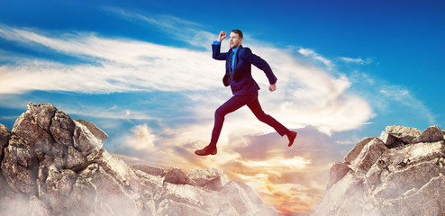 Businessman jumping through the gap among mountains.