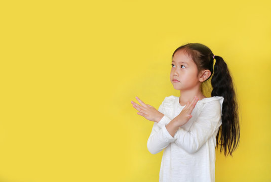 Portrait of young asian child girl crossed his hands isolated on yellow background with copy space. Kid shows Stop sign or making X sign her arms gesture and looks up. Said no.