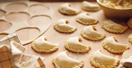 Raw dumplings with cheese and potato filling prepared for cooking on a wooden board, close-up view. 