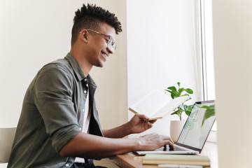 Positive smiling african guy using laptop computer.