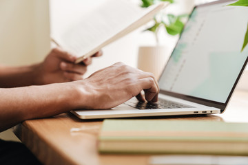 Young african guy using laptop computer holding notebook.
