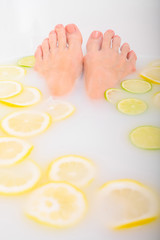 Girl takes a milk bath with lemons and limes. Citrus spa. Body care. Skin whitening. Women's feet.