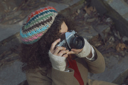 Curly haired photographer woman holding her camera in the park and shooting