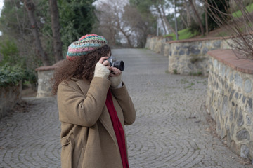 Curly haired photographer woman holding her camera in the park and shooting