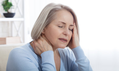 Woman suffering from stress or a headache grimacing in pain as she holds the back of her neck with her other hand to her temple, with copyspace. Concept photo with indicating location of pain.