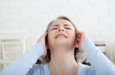 Woman suffering from stress or a headache grimacing in pain as she holds the back of her neck with her other hand to her temple, with copyspace. Concept photo with indicating location of pain.