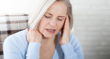 Woman suffering from stress or a headache grimacing in pain as she holds the back of her neck with her other hand to her temple, with copyspace. Concept photo with indicating location of pain.