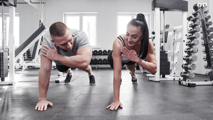 Muscular sexy man and woman push up on one arm in gym