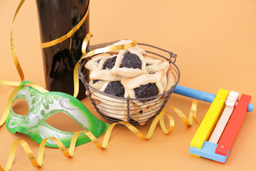 Tasty hamantaschen, gragger and party decor for Purim holiday and bottle of wine on color background
