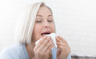 Healthcare, cold, allergy and people concept, sick woman blowing her runny nose in paper tissue on...