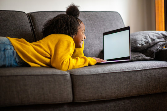 african american girl lying on sofa looking at laptop computer screen at home