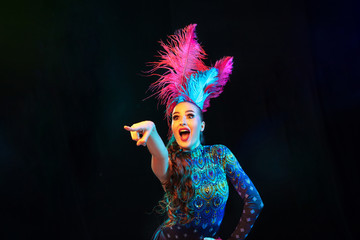 Pointing. Beautiful young woman in carnival, stylish masquerade costume with feathers on black...