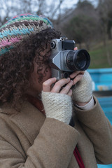 Curly haired photographer woman holding her camera in the park and shooting