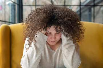 Young woman with curly hair looks thoughtful in a cafe