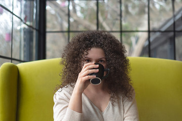 Young woman with curly hair is drinking coffee in a cafe
