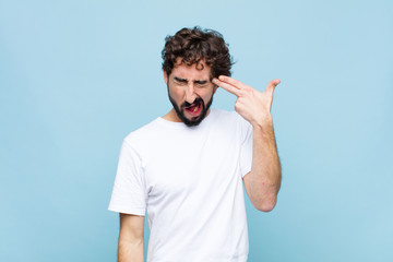 young crazy bearded man looking unhappy and stressed, suicide gesture making gun sign with hand,...