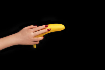 Beautiful female hand with trendy red manicure holding banana like a gun on isolated black background. Mockup for your design. Creative trendy flat lay with space for text.