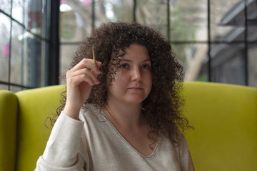 Young woman with curly hair smokes a cigarette in a cafe