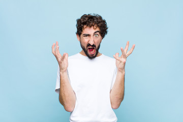 young crazy bearded man screaming with hands up in the air, feeling furious, frustrated, stressed...
