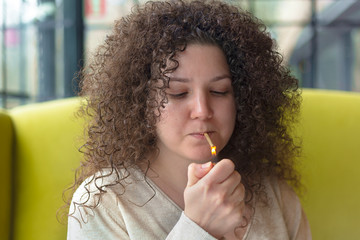 Young woman with curly hair smokes a cigarette in a cafe