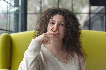 Fototapeta na wymiar Young woman with curly hair smokes a cigarette in a cafe