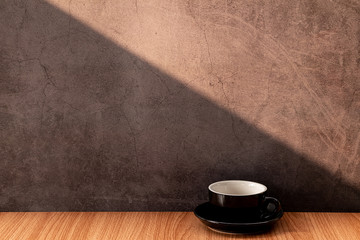 Black coffee mugs on a wooden table with light and shadow on old gray concrete walls.