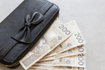 The home budget in the hands of women in Poland - symbol. A beautiful black bag with a bow full of Polish money.