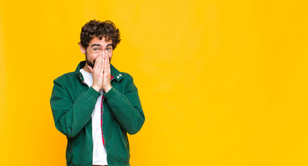 young crazy bearded man looking happy, cheerful, lucky and surprised covering mouth with both hands...