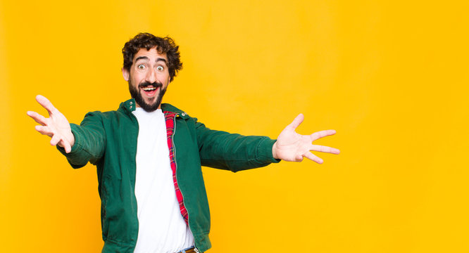 young crazy bearded man smiling cheerfully giving a warm, friendly, loving welcome hug, feeling happy and adorable against flat wall