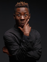 Fototapeta premium Emotional portrait of a young African man in black clothing against a dark background. Studio photography.