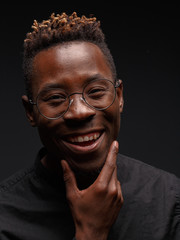 Emotional portrait of a young African man in black clothing against a dark background. Studio photography.