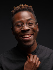 Emotional portrait of a young African man in black clothing against a dark background. Studio photography.
