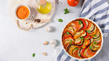Ratatouille casserole on wooden background. Colorful layers of fresh summer vegetables: zucchini, eggplant, tomatoes and potatoes. Healthy vegan, vegetarian dish. Top view, copy space. Menu, recipe