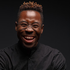 Emotional portrait of a young African man in black clothing against a dark background. Studio photography.