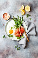 Green asparagus with fried egg, fresh oregano leaves and prosciutto on the plate. Top view.